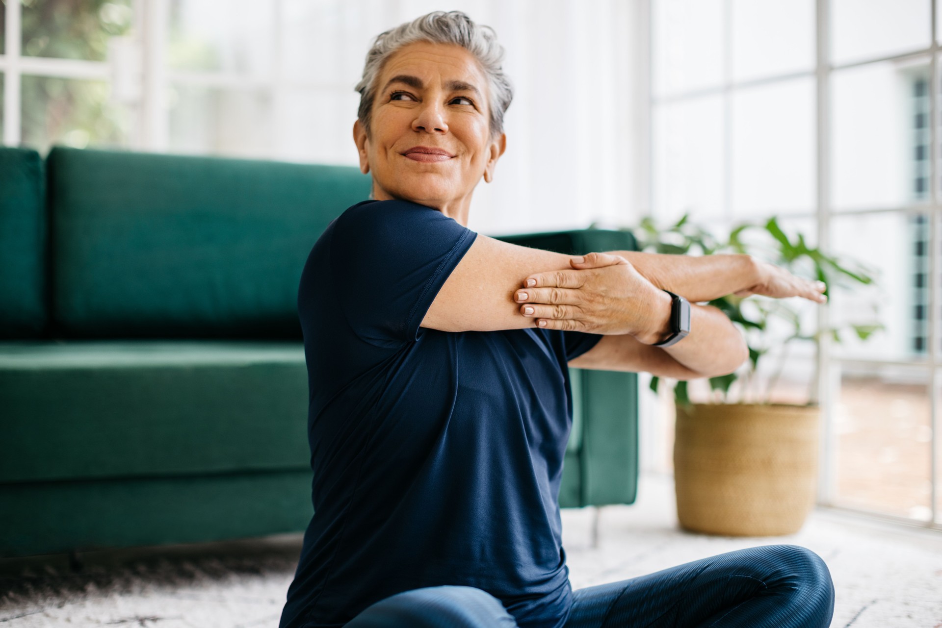 Happy and healthy senior woman doing a cross arm stretch in a peaceful yoga session at home